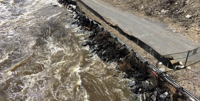 Flooding water eroding a river bank next to a road.